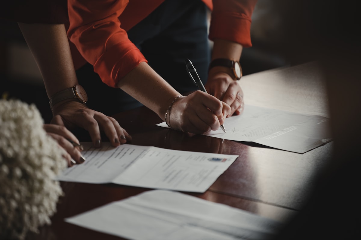 Deux personnes signent des documents administratifs sur un bureau en bois