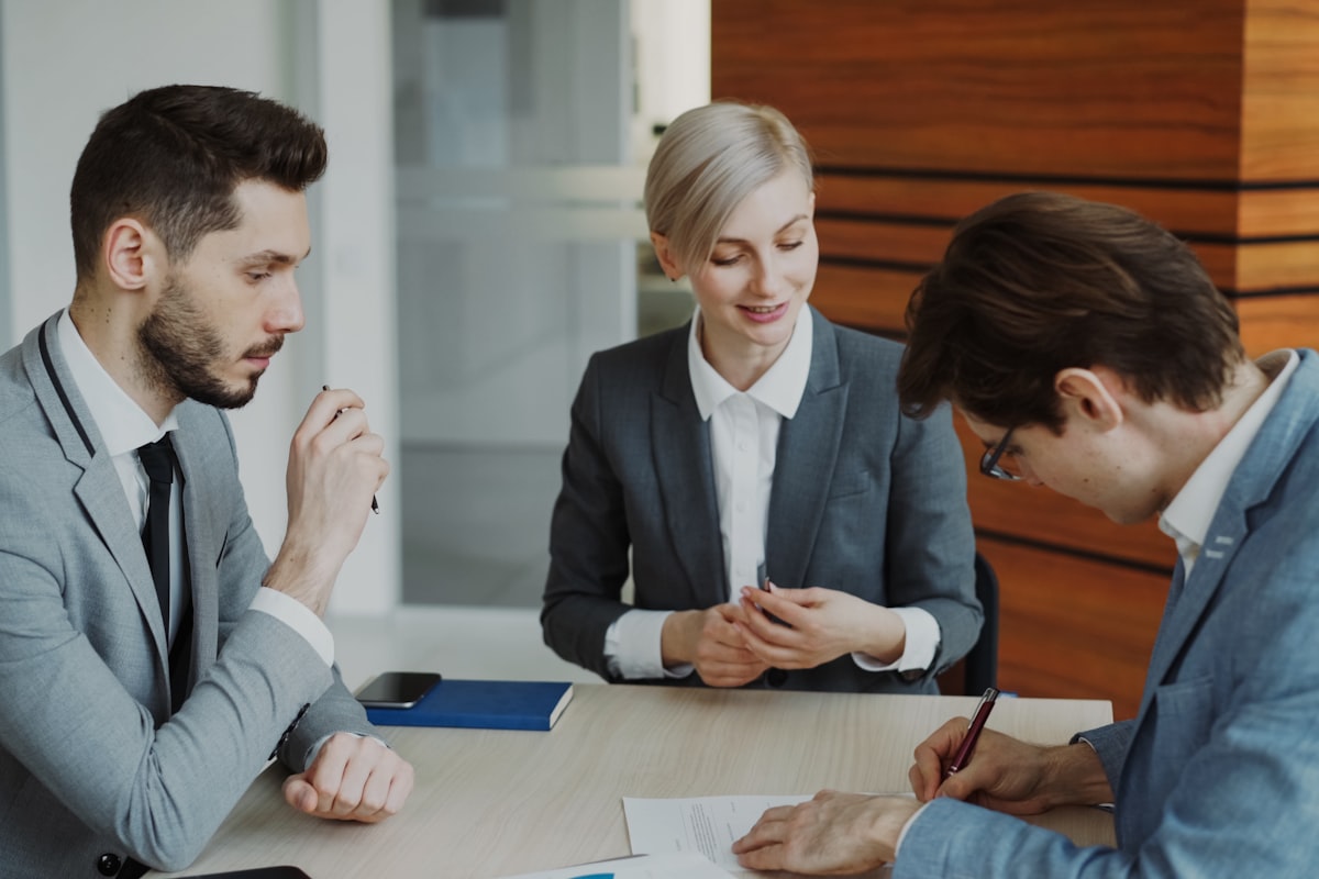Trois professionnels en costume signent un document autour d'une table